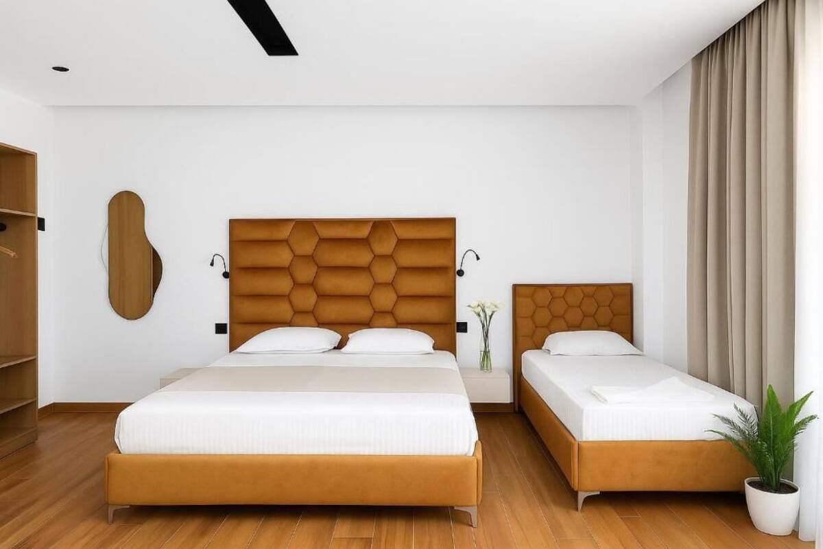 A hotel room with a large bed, a smaller bed, a wardrobe, and a potted plant.