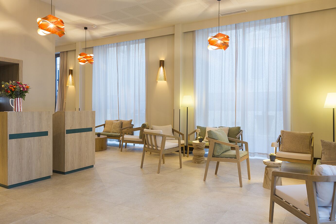 A hotel lobby with a reception desk, seating area, and large windows with sheer curtains.