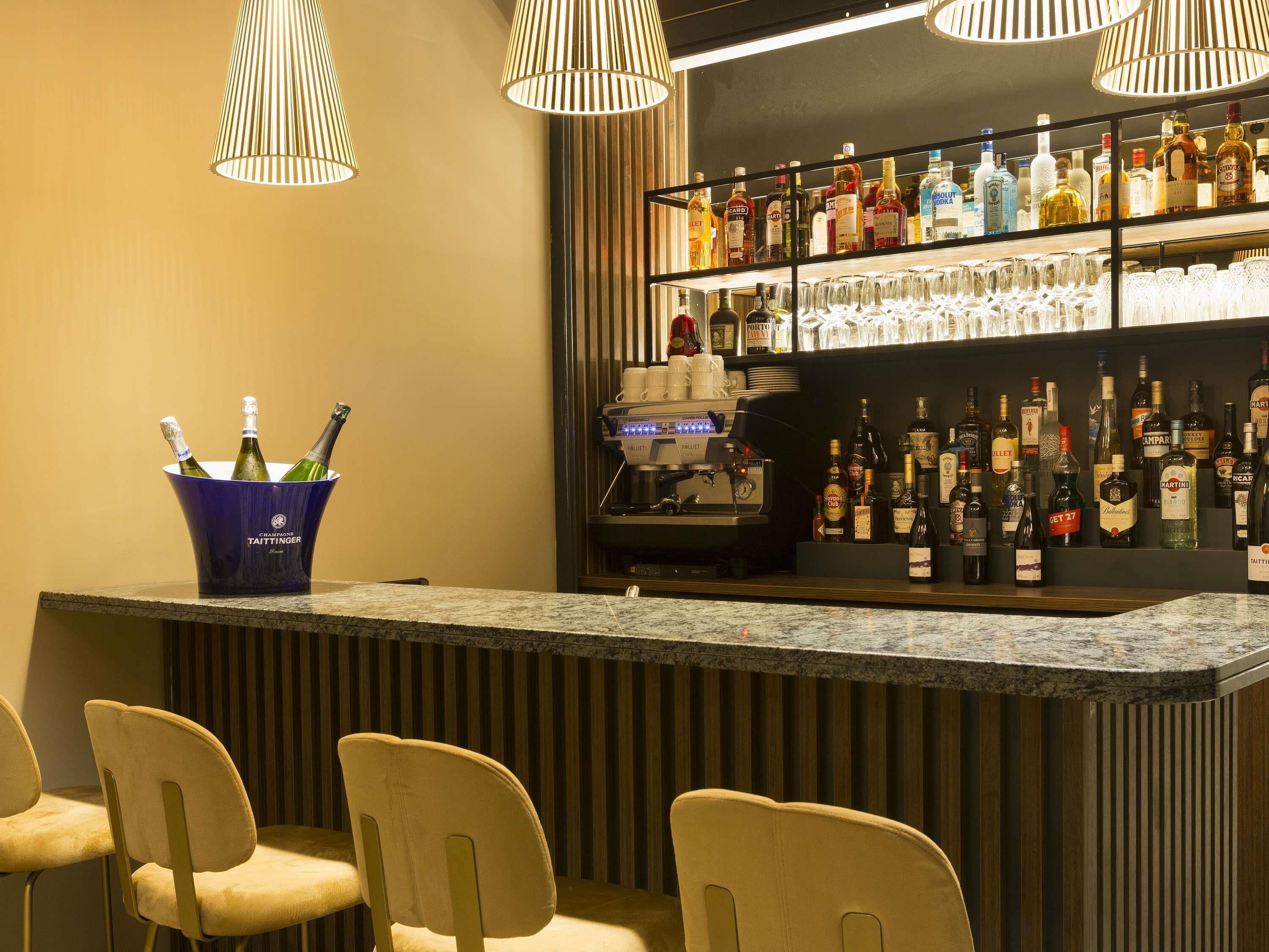 A bar area with a counter, bar stools, a coffee machine, and shelves stocked with bottles and glasses.