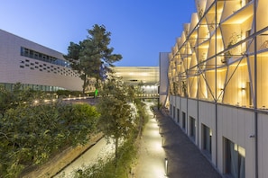 A modern building with a glass facade, a landscaped pathway, and a tree in the foreground. - Mercure Nîmes Centre Arènes (Nimes)