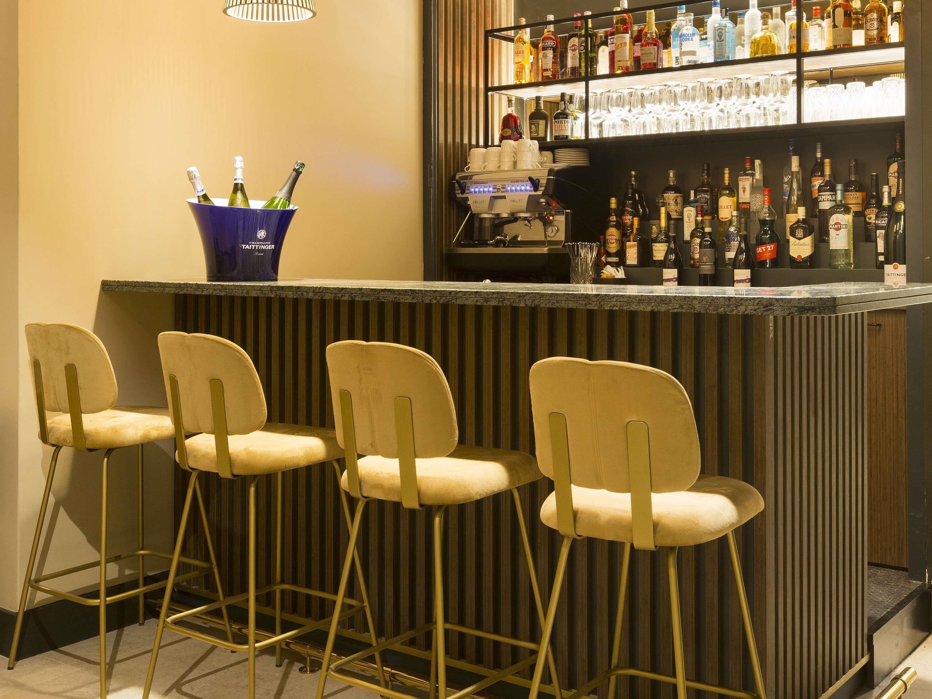 Zona de bar con mostrador, taburetes y una variedad de botellas y vasos.