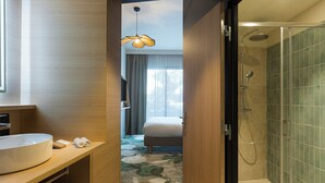 A modern bathroom with a large sink, shower, and a bed visible through an open door. - Mercure Nîmes Centre Arènes (Nimes)