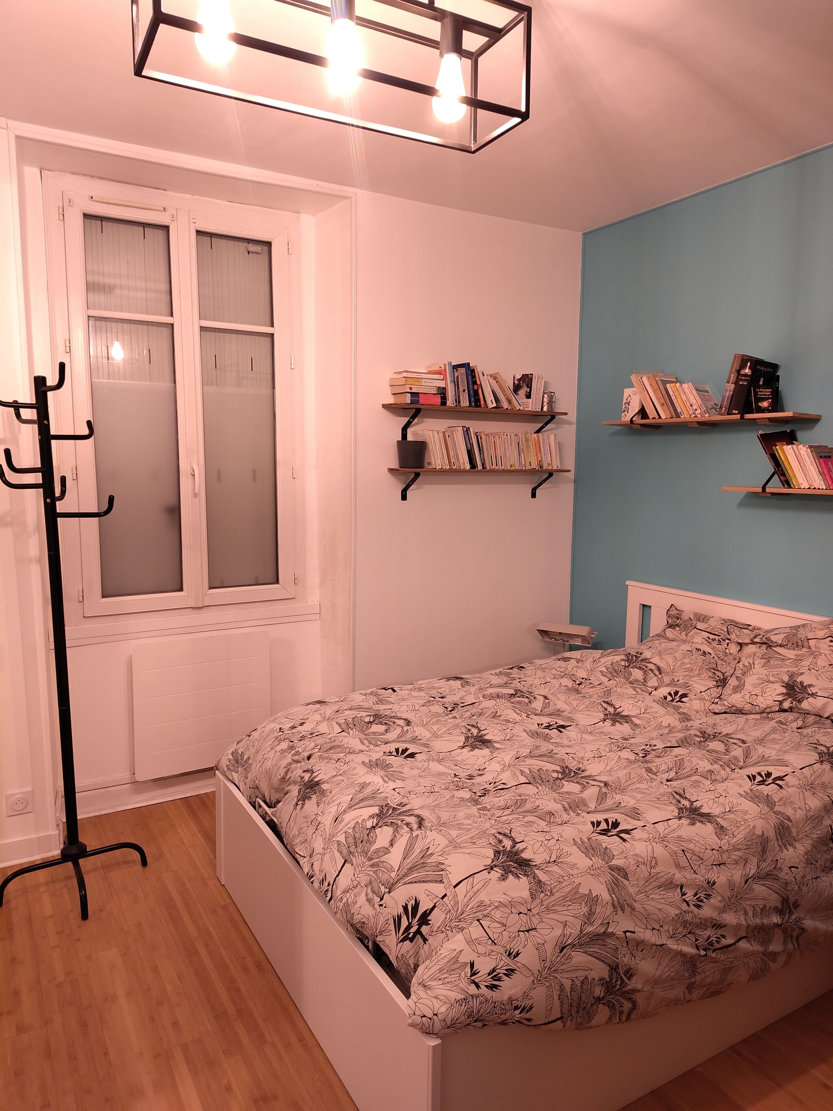 A bedroom with a bed, a radiator, a window with frosted glass, and two bookshelves with books.