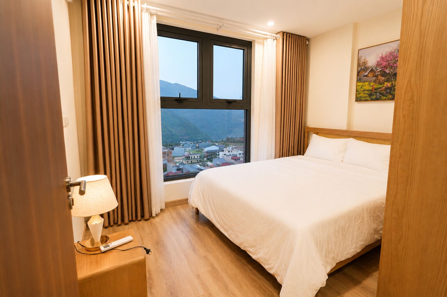 A hotel room with a bed, a window with curtains, a lamp, and a painting on the wall.