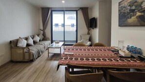Uma sala de estar com sofá, mesa de centro, mesa de jantar com cadeiras, televisão e um quadro na parede.