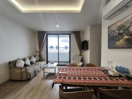Una sala de estar con sofá, mesa de centro, mesa de comedor con sillas, televisor y un cuadro en la pared.
