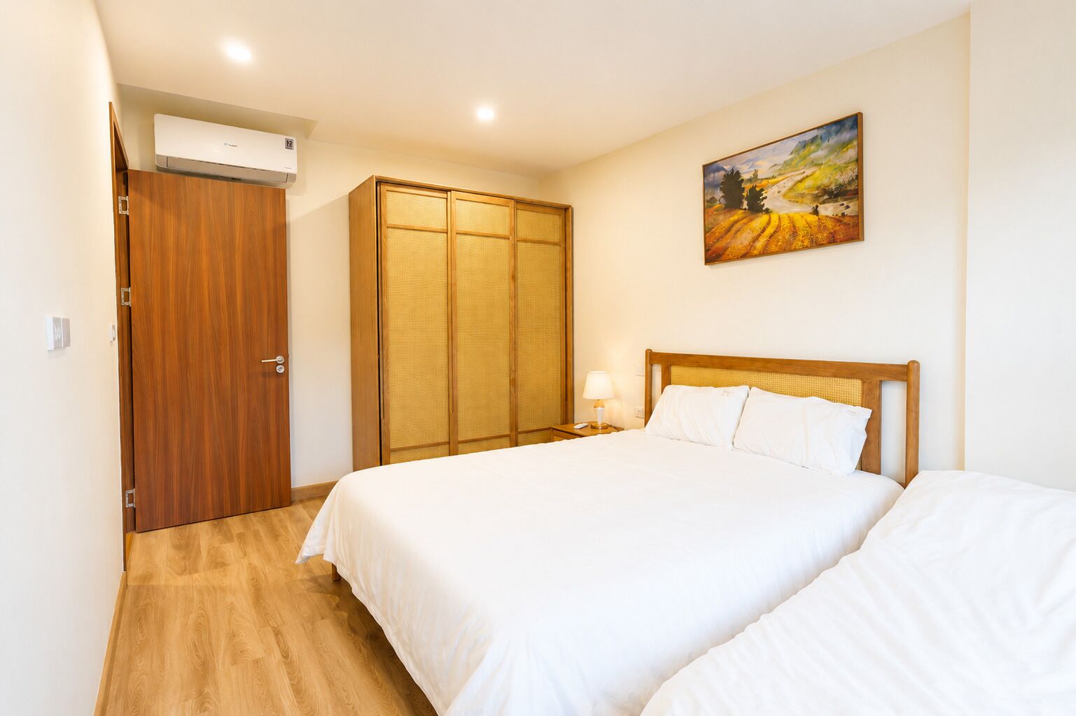 Una camera d'albergo con un'armadiatura in legno, un letto con biancheria bianca, un comodino con una lampada e un quadro appeso al muro.