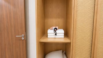 A wooden wardrobe with a shelf holding folded towels and a black object.