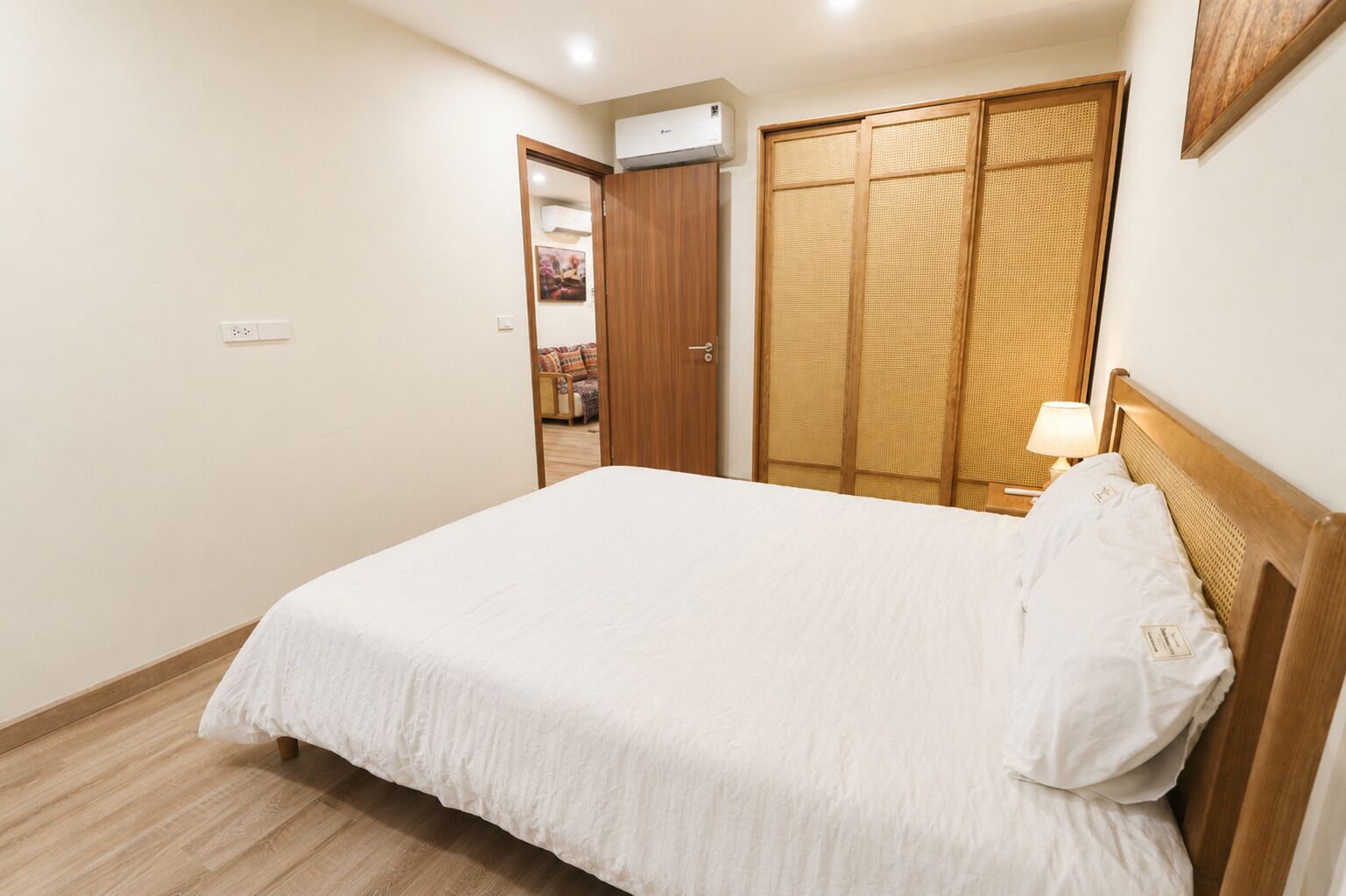 A bedroom with a bed, a wooden headboard, a bedside lamp, and a wardrobe with a woven door.