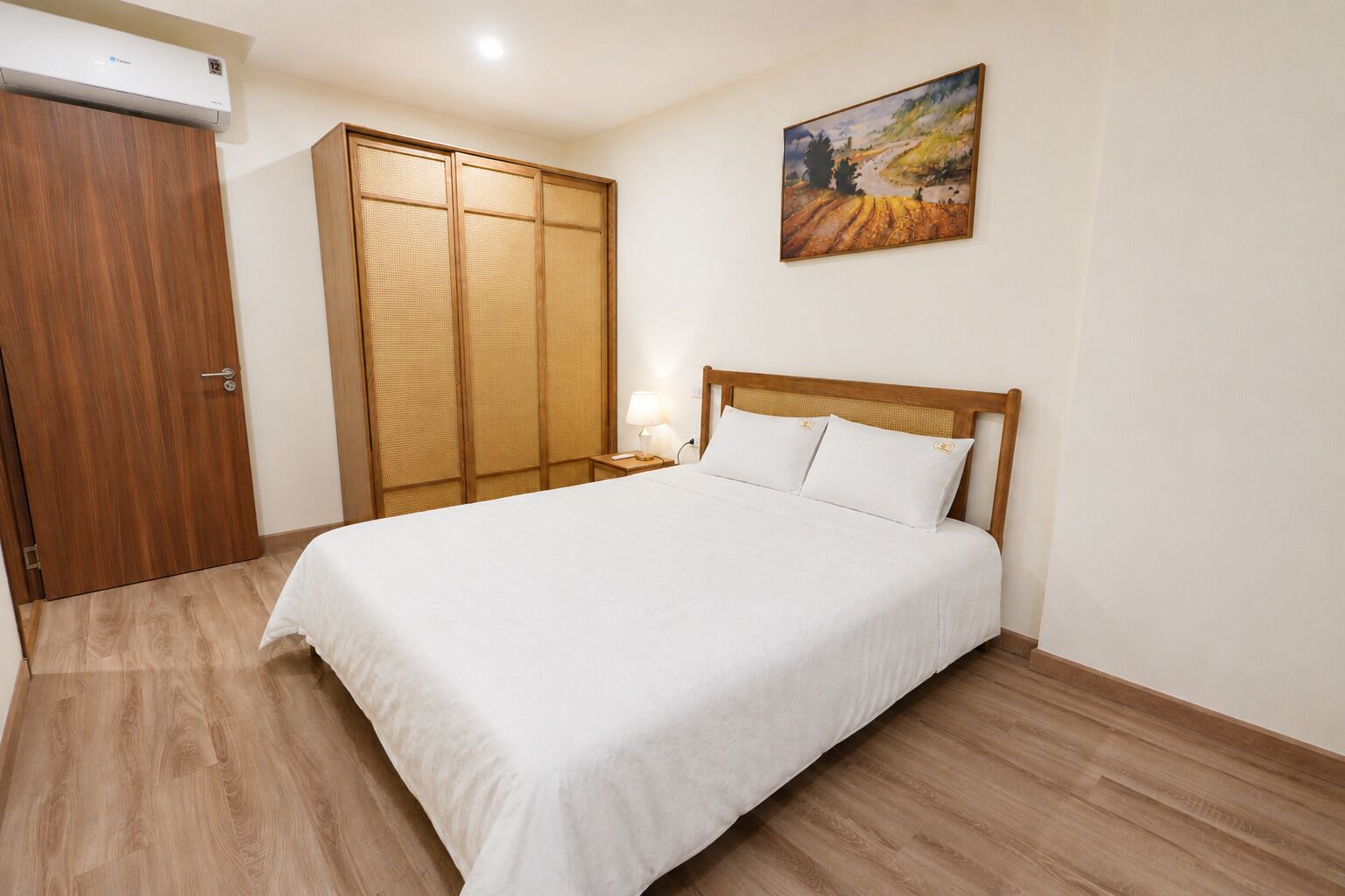 A bedroom with a bed, wooden wardrobe, and a painting on the wall.