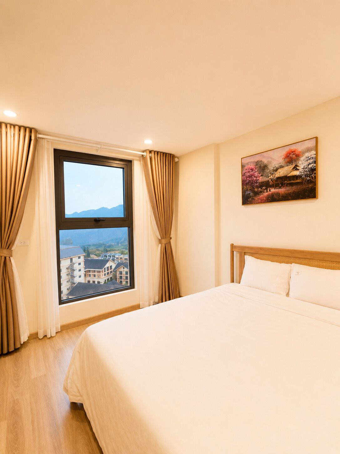Quarto de hotel com uma cama grande, janela com cortinas, um quadro na parede e vista para prédios.