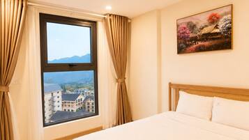 Quarto de hotel com uma cama grande, janela com cortinas, um quadro na parede e vista para prédios.