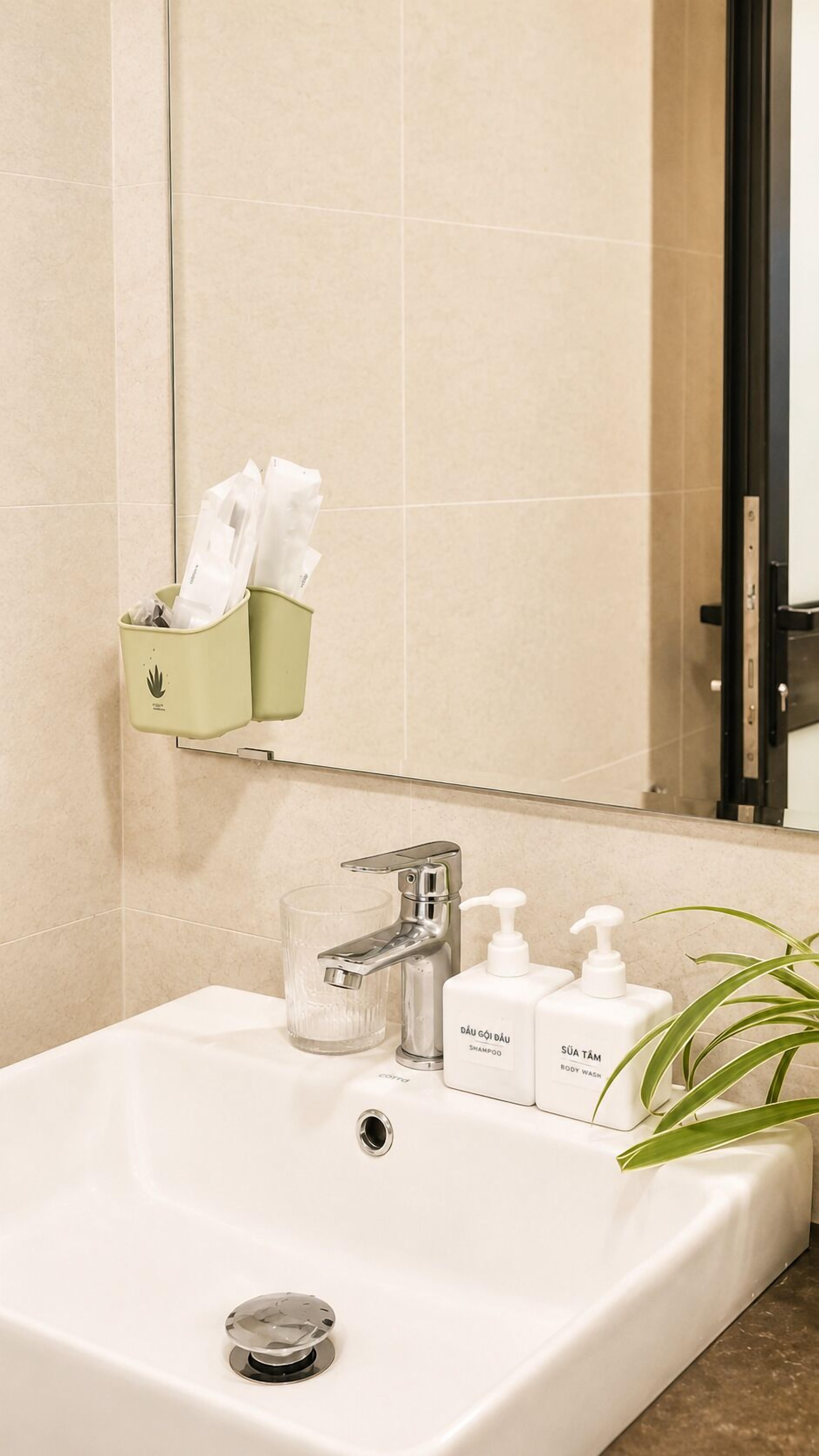 A bathroom with a white sink, a mirror, a green wastebasket, and two bottles of shampoo and body wash.