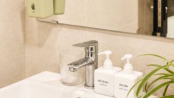 A bathroom with a white sink, a mirror, a green wastebasket, and two bottles of shampoo and body wash.
