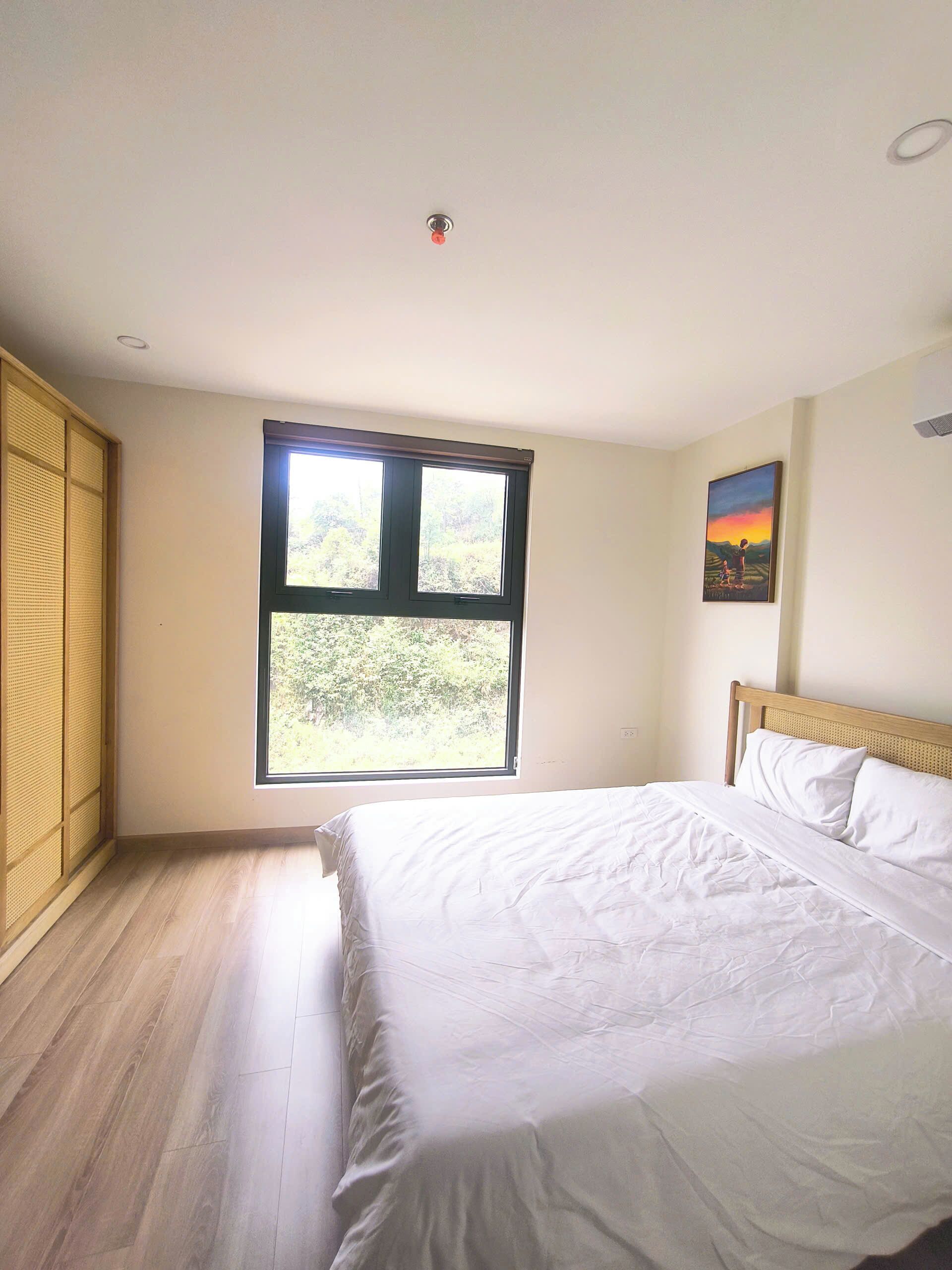 A bedroom with a bed, a window, and a painting on the wall.