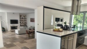 Une cuisine moderne dotée d’un grand îlot central, un coin repas avec une table et des chaises, un salon avec un canapé et une télévision, et une cheminée.
