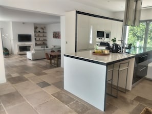 Eine moderne Küche mit einer großen Kochinsel, ein Essbereich mit Tisch und Stühlen, ein Wohnzimmer mit Sofa und Fernseher sowie ein Kamin.
