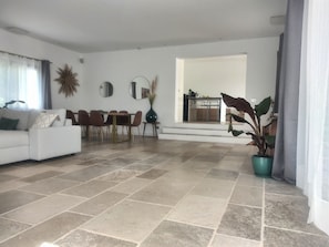 Ein geräumiger Wohnbereich mit einer Couch, einem Esstisch, Stühlen, einer Topfpflanze und einer Küche im Hintergrund.