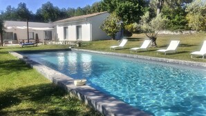 Une piscine bordée de pierres, entourée de pelouse et d’arbres.