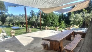 Une terrasse extérieure avec une table et des bancs en bois, entourée d’un sol en pierre et d’un auvent.