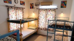 A dormitory room with bunk beds, floral curtains, a clock, and an air conditioning unit. - The Sheltor (Chennai)