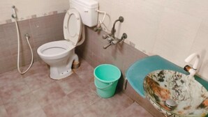 A bathroom with a toilet, a bucket, and a sink. - The Sheltor (Chennai)