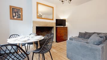 A living room with a fireplace, a dining table set for four, and a grey sofa.