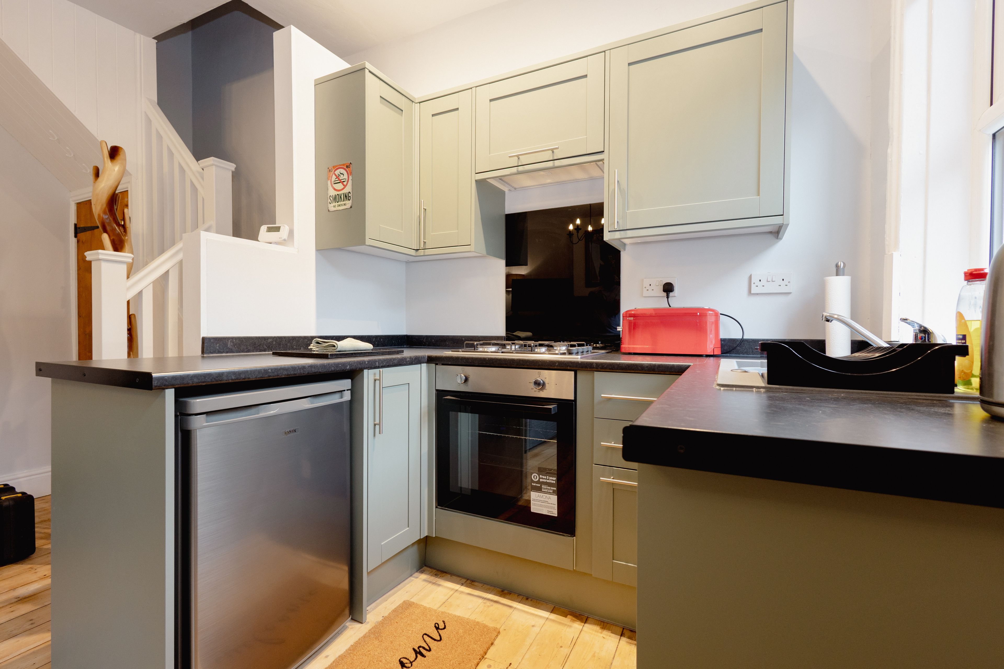 Une cuisine moderne avec des meubles de couleur claire, un four encastré et un grille-pain rouge.