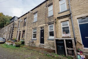 A row of terraced houses with brick facades, a car parked on the street, and a garden area with potted plants.