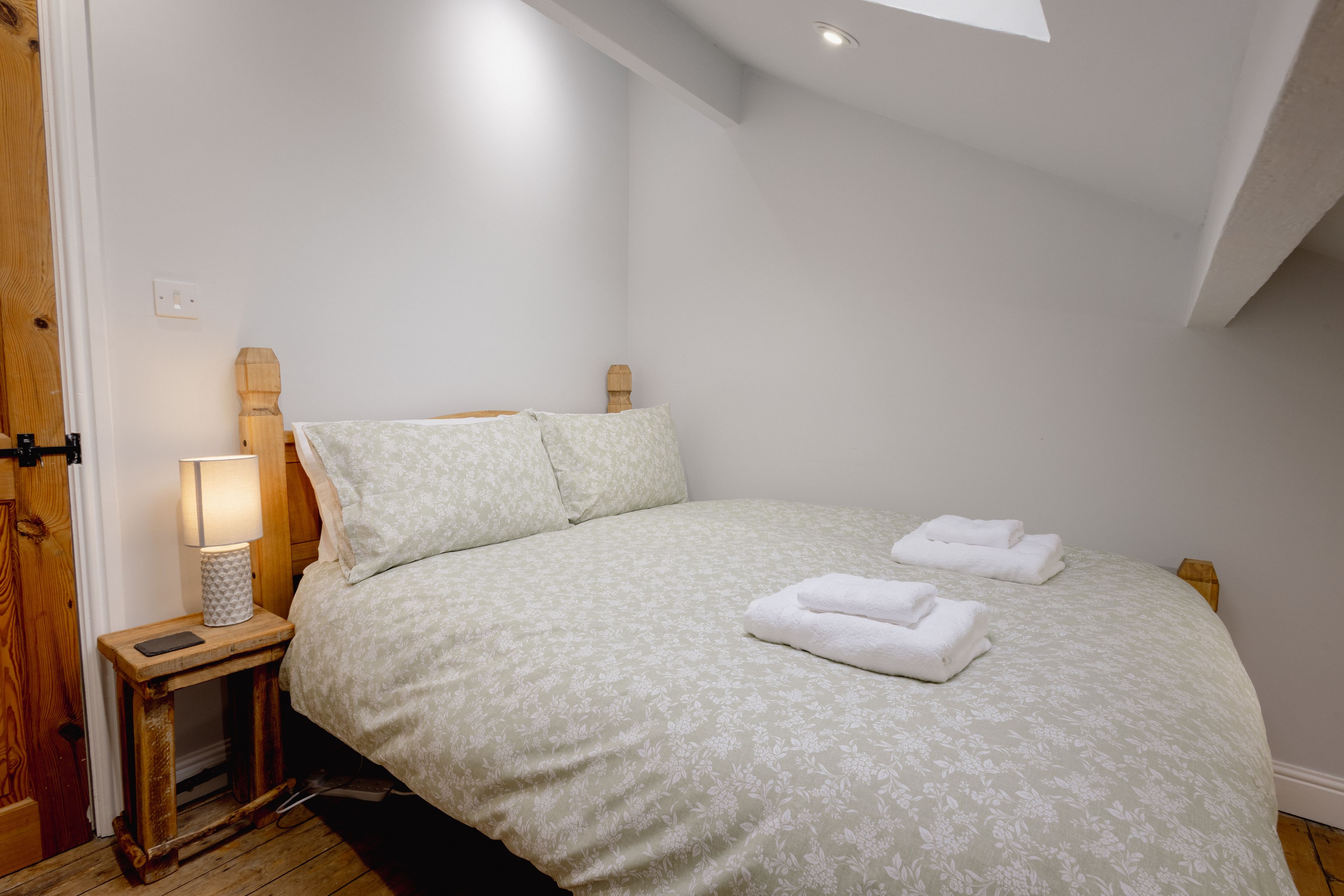 Ein Schlafzimmer mit einem Bett, Kissen, einem Nachttisch mit Lampe und einem gefalteten Handtuch.