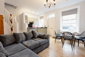 A modern living room with a sectional sofa, dining table with chairs, and a kitchen in the background.