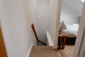 A narrow stairway leading to a bedroom with a bed, a bedside table, and a lamp.