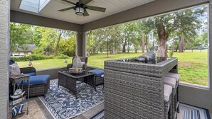 Ein überdachter Patio-Bereich mit Korbmöbeln, einem Deckenventilator und Blick auf einen Rasen.