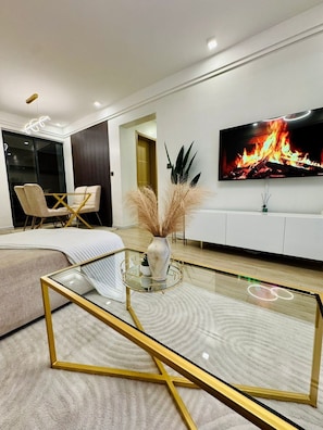 A modern living room with a sofa, a glass coffee table with gold frame, a TV displaying a fire, and a plant. - 2-bedroom apartment in peaceful Syokimau near airport with Free parking (Nairobi)