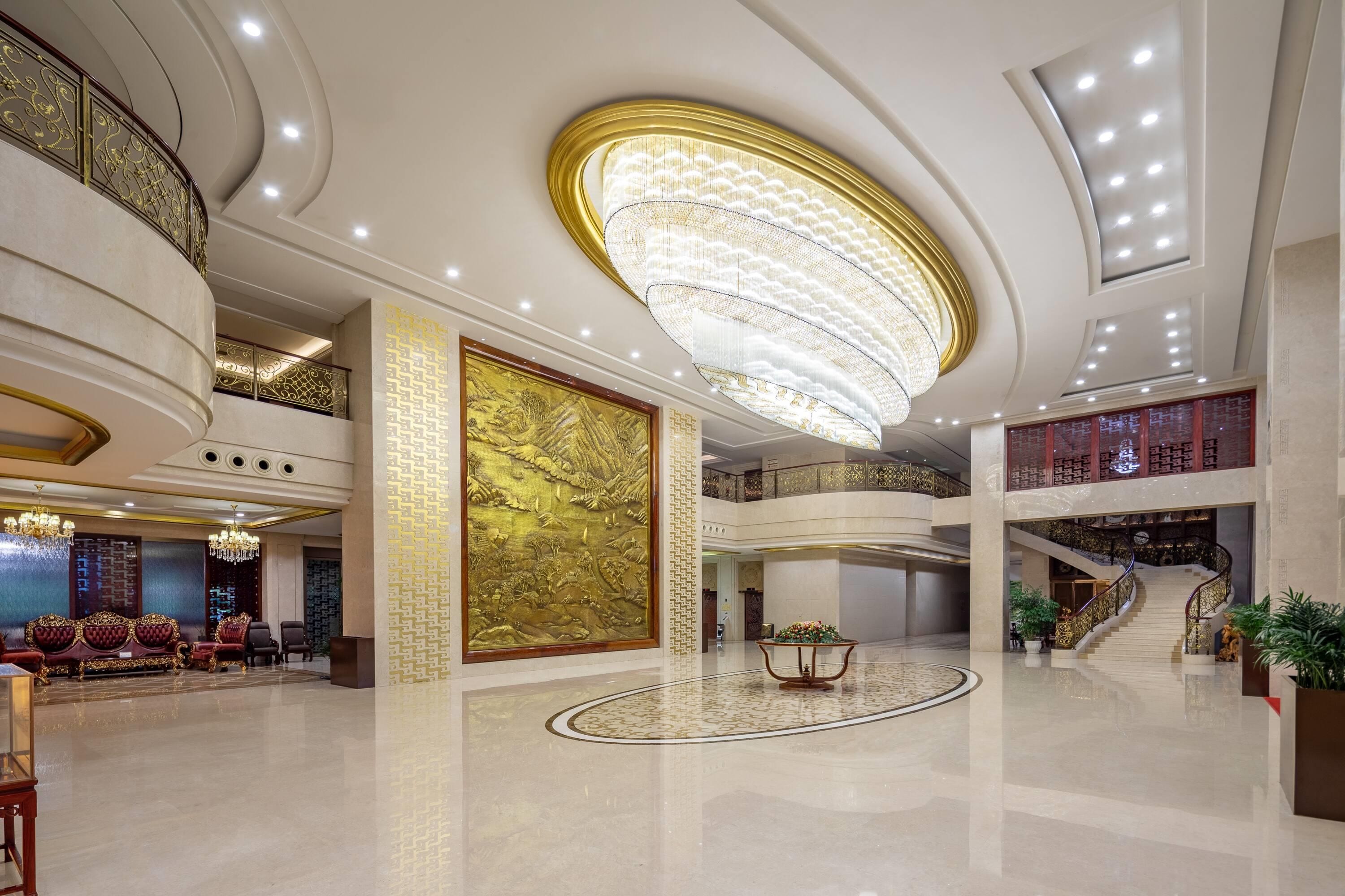 A spacious lobby with a grand chandelier, a high ceiling, and a staircase leading to an upper level.
