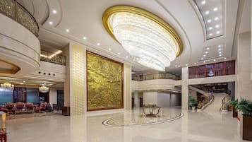 A spacious lobby with a grand chandelier, a high ceiling, and a staircase leading to an upper level.