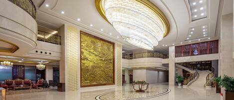 A spacious lobby with a grand chandelier, a high ceiling, and a staircase leading to an upper level.