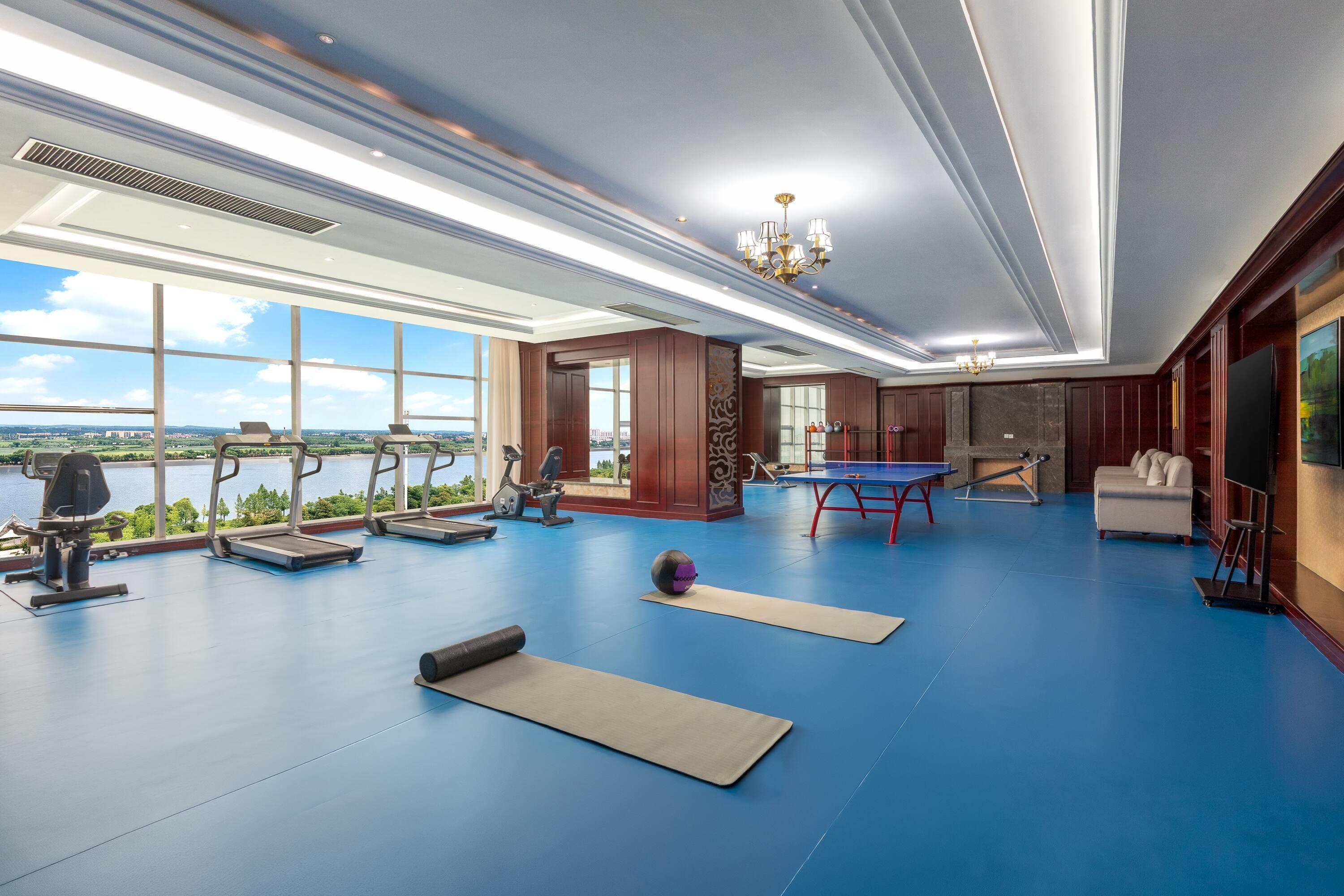Una habitación amplia con equipo de ejercicio, una mesa de ping pong y grandes ventanales que ofrecen vistas a un cuerpo de agua.