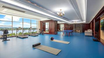 Una habitación amplia con equipo de ejercicio, una mesa de ping pong y grandes ventanales que ofrecen vistas a un cuerpo de agua.