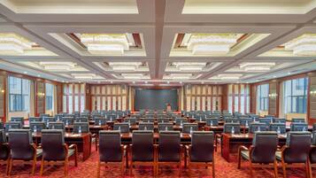 A large conference room with rows of tables and chairs, a stage at the front, and a patterned carpet.