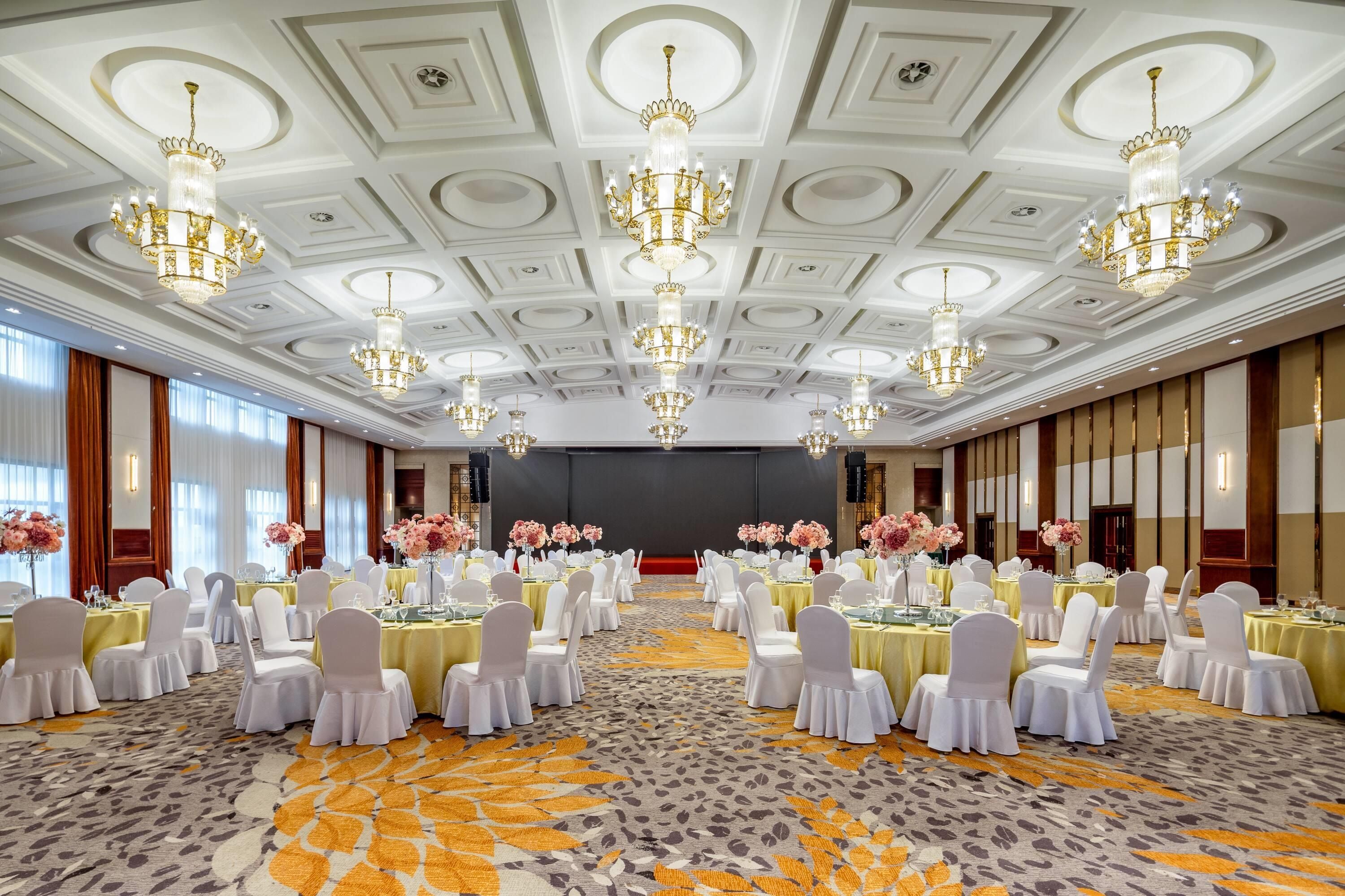 Un salón de banquetes con mesas redondas, sillas blancas y candelabros.