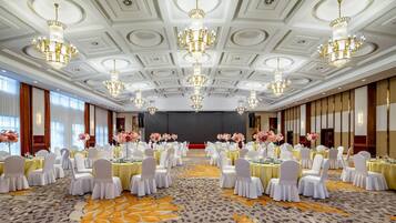 Un salón de banquetes con mesas redondas, sillas blancas y candelabros.