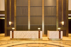 A reception desk with a marble finish, flanked by vertical wooden panels and two wall-mounted lamps. - Genpla Hotel by Shenzhen Metro (Shenzhen)