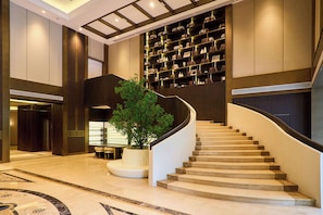 A grand staircase with a curved design, a large potted plant, and a wall of bookshelves. - Genpla Hotel by Shenzhen Metro (Shenzhen)
