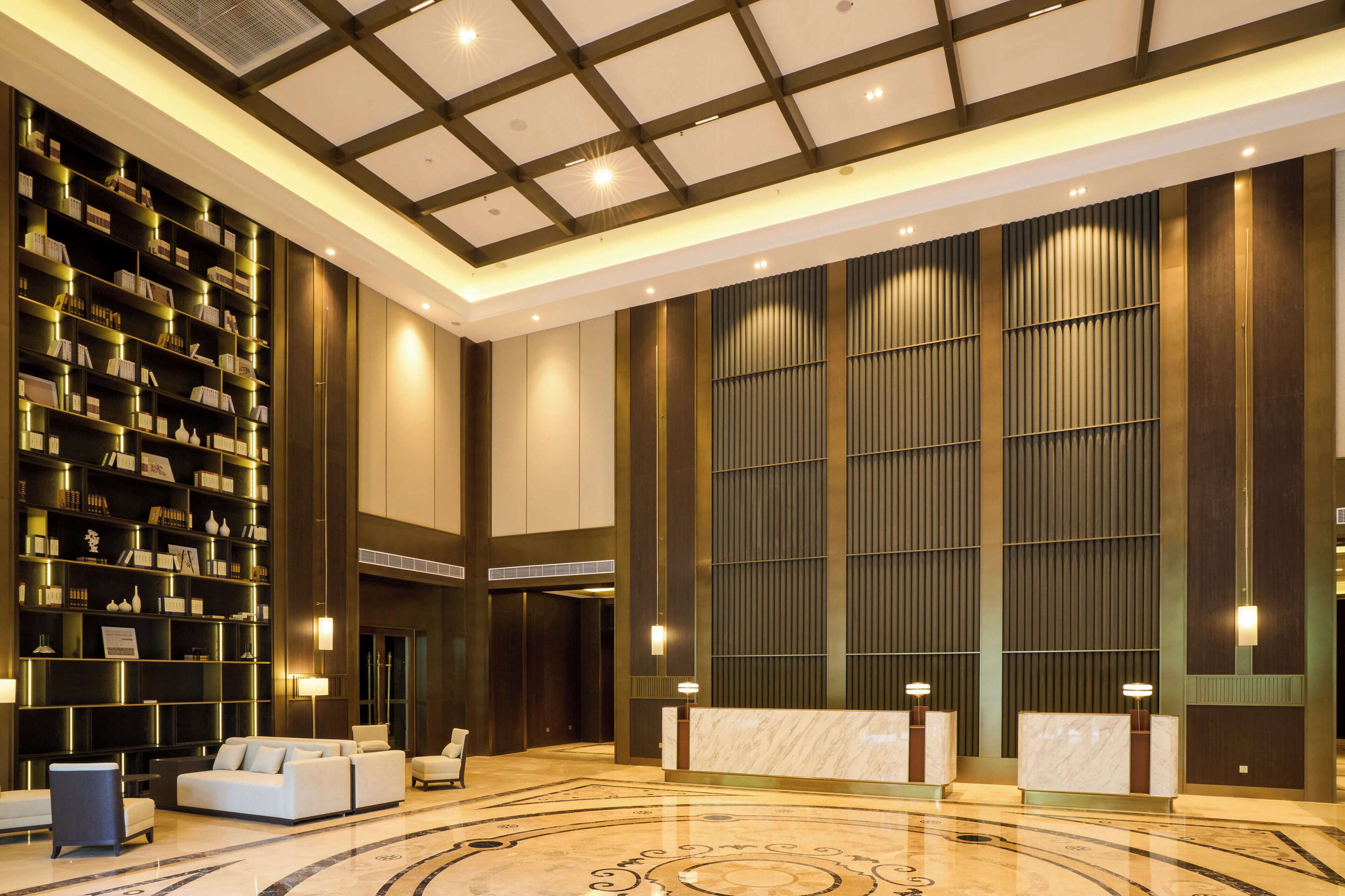 A spacious lobby with a high ceiling, a large bookshelf, a reception desk, and a seating area.