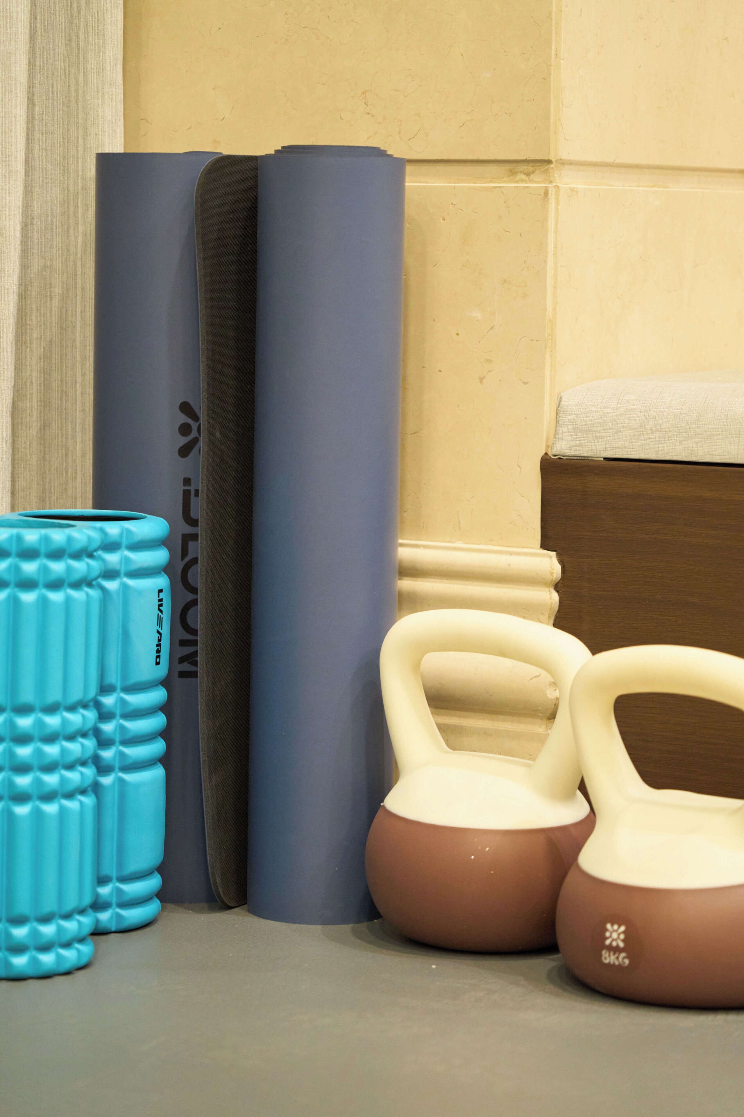 A set of exercise equipment including a blue foam roller, a brown kettlebell, and a pair of dumbbells.