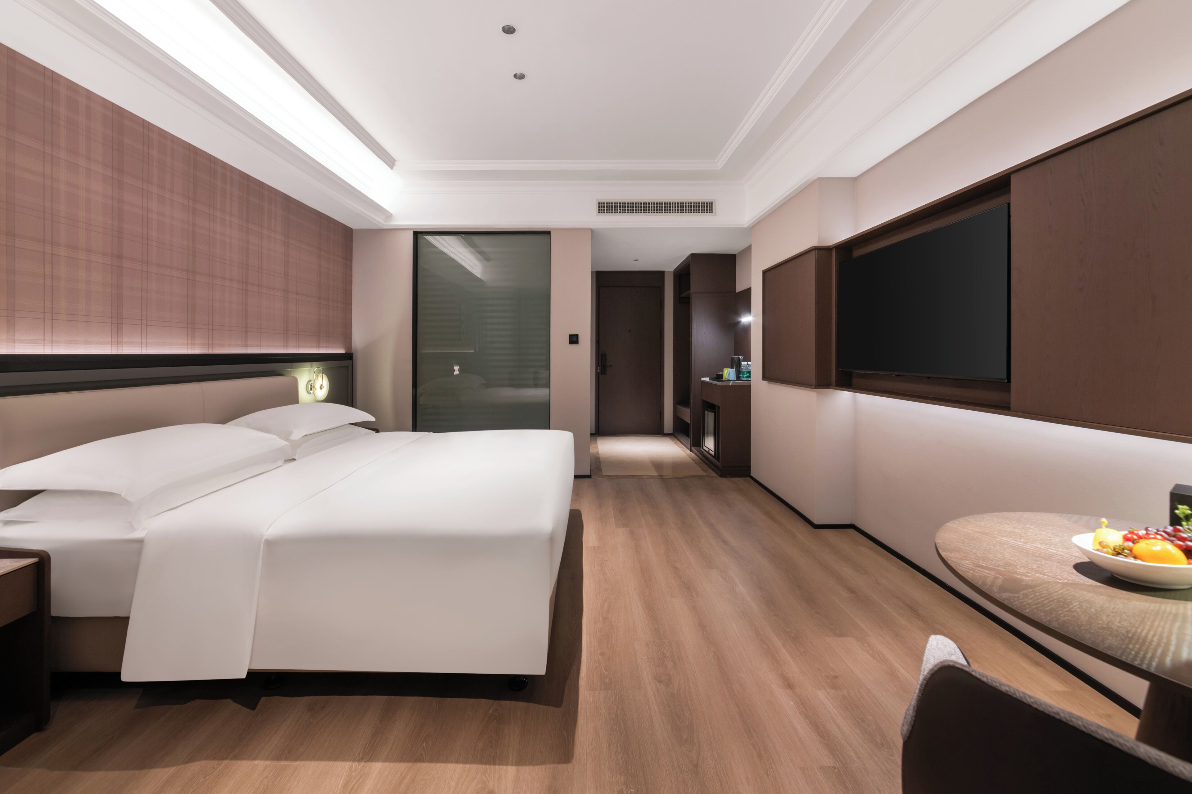 Ein modernes Hotelzimmer mit einem großen Bett, einem Esstisch mit Obst und einem Fernseher.