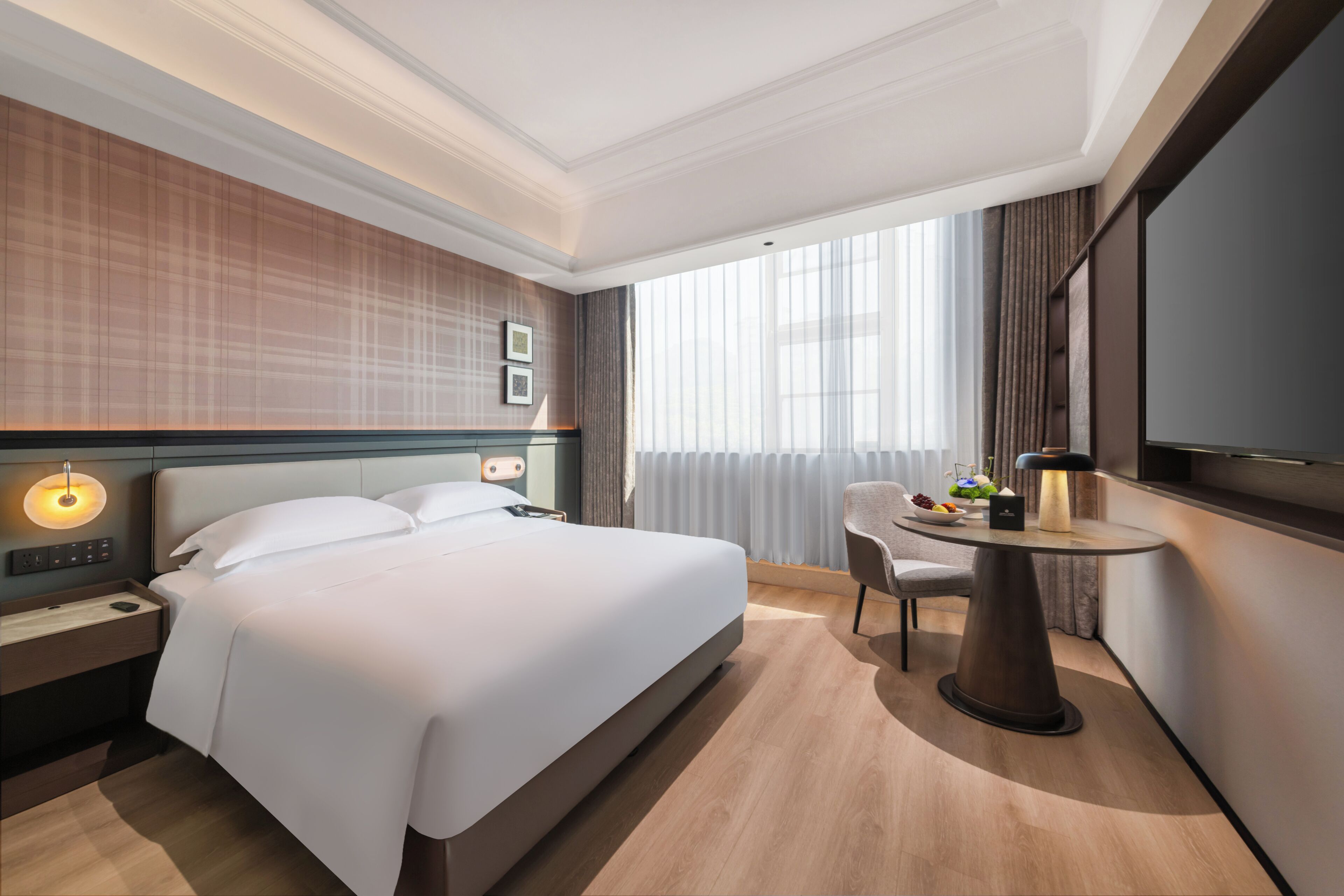 Una habitación de hotel con cama, mesita de noche, lámpara, sillón y televisor.