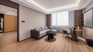 A modern hotel room with a sofa, a round coffee table, a dining table, and a TV. - Genpla Hotel by Shenzhen Metro (Shenzhen)