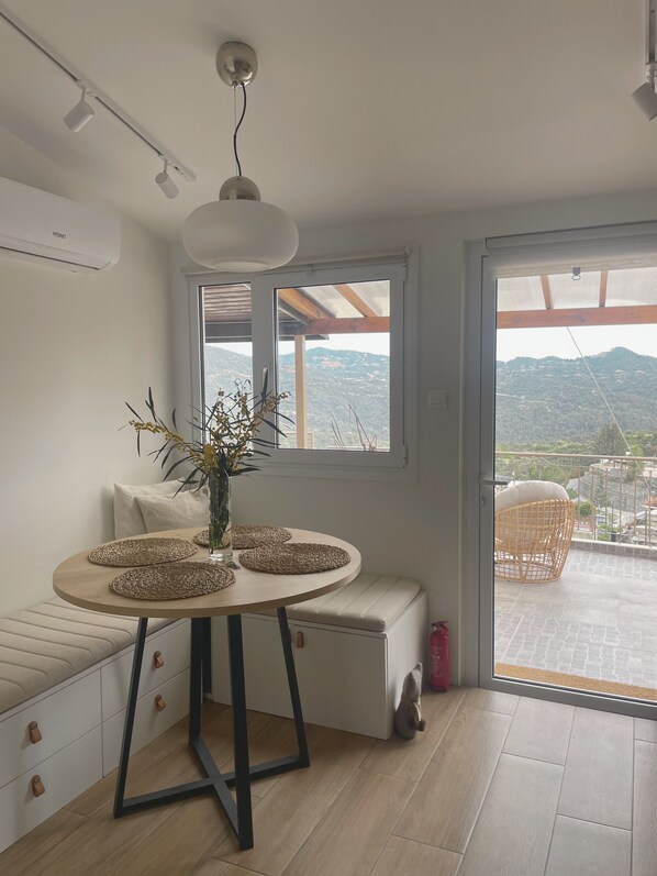 Ein modernes Interieur mit einem runden Tisch, einer Vase mit Zweigen, einer Bank und Blick auf einen Balkon mit Gartenmöbeln.